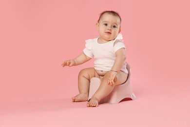 Photo of Cute little baby sitting on potty against pink background