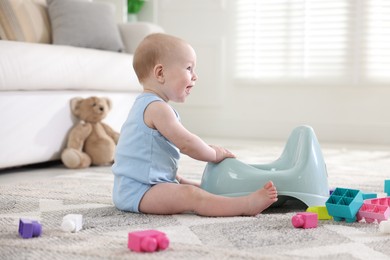 Photo of Cute little baby sitting near potty and toys at home