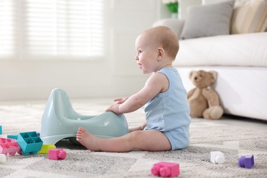 Photo of Cute little baby sitting near potty and toys at home