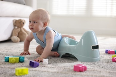 Photo of Cute little baby sitting near potty and toys at home