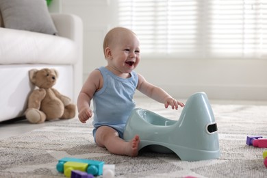 Photo of Cute little baby sitting near potty and toys at home