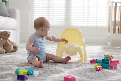 Photo of Cute little baby with teether sitting near potty at home