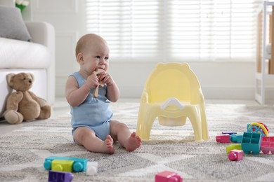 Photo of Cute little baby with teether sitting near potty at home