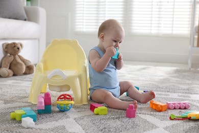Photo of Cute little baby with toy sitting near potty at home