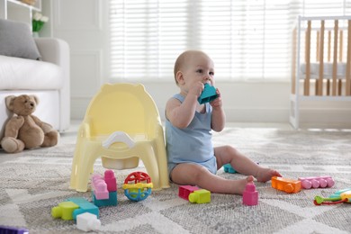 Photo of Cute little baby with toy sitting near potty at home
