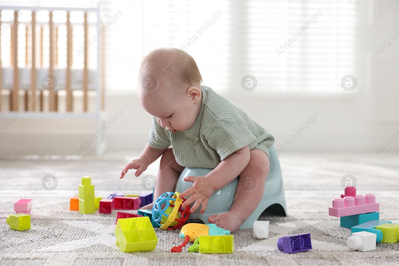Photo of Cute little baby sitting on potty and toys at home