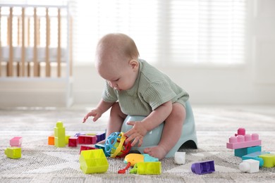 Photo of Cute little baby sitting on potty and toys at home