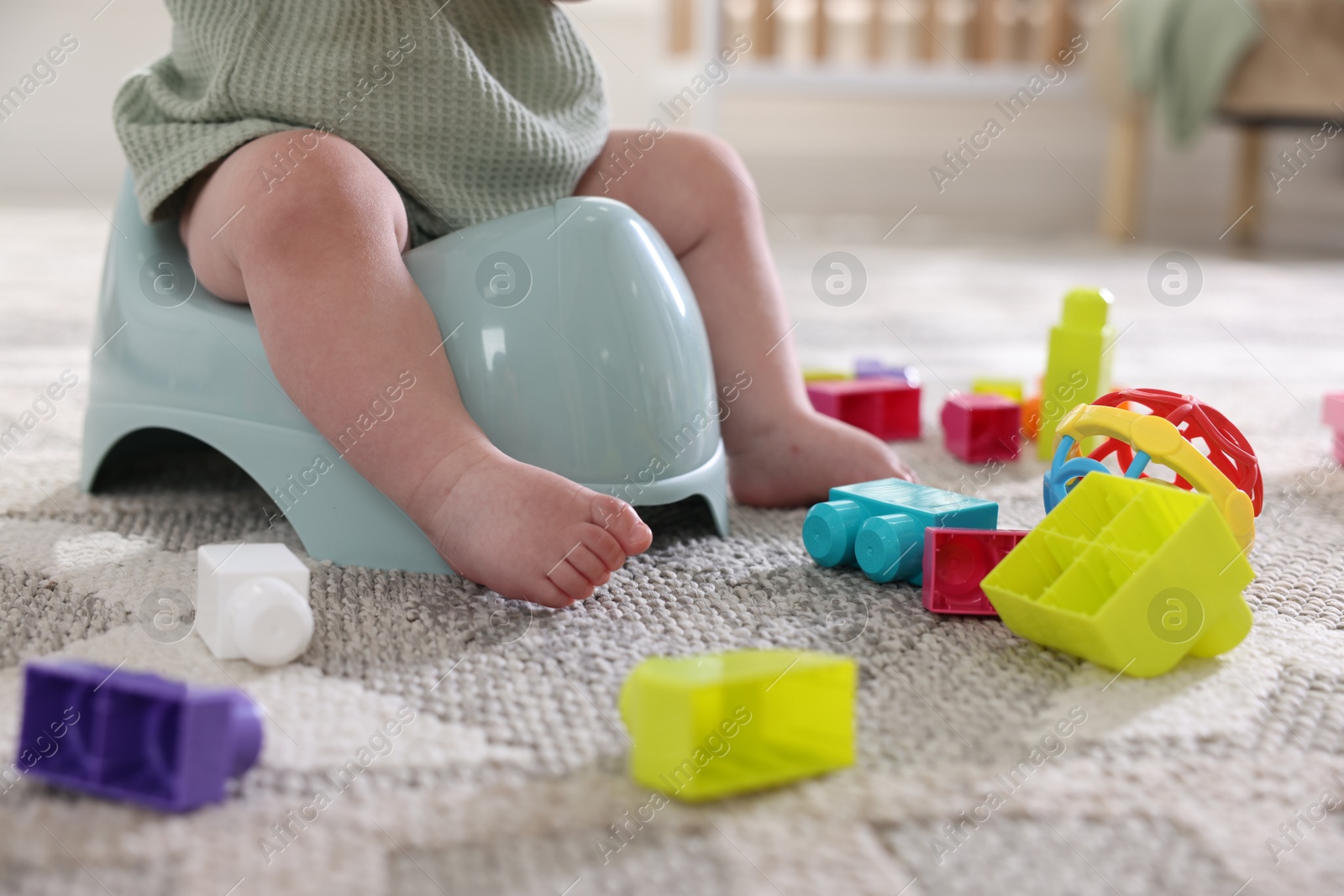 Photo of Cute little baby sitting on potty and toys at home, closeup
