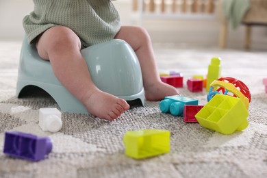 Photo of Cute little baby sitting on potty and toys at home, closeup