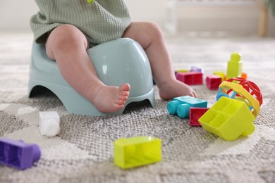 Photo of Cute little baby sitting on potty and toys at home, closeup