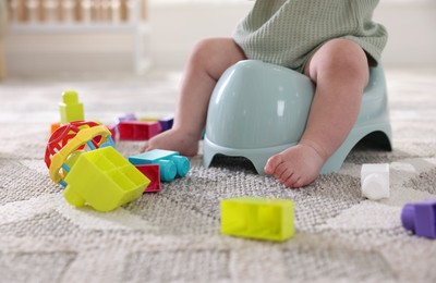 Photo of Cute little baby sitting on potty and toys at home, closeup