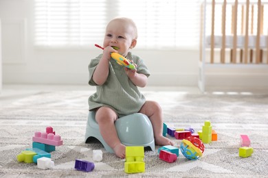 Photo of Cute little baby with toy sitting on potty at home