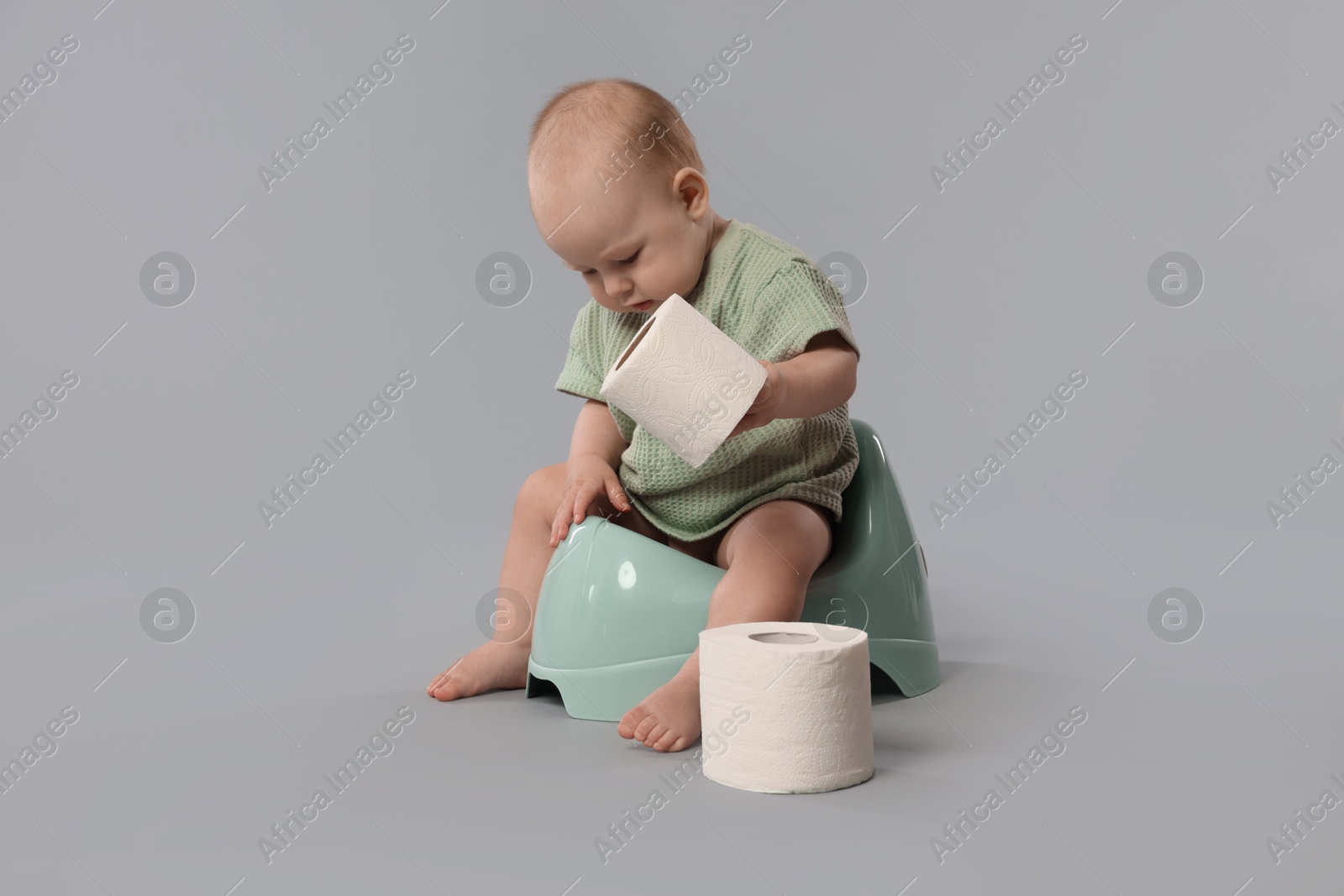 Cute little baby sitting on potty and rolls of toilet paper against light grey background Photo of Cute little baby sitting on potty and rolls of toilet paper against light grey background