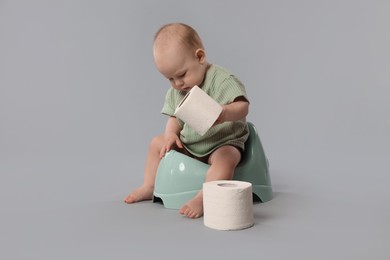 Photo of Cute little baby sitting on potty and rolls of toilet paper against light grey background
