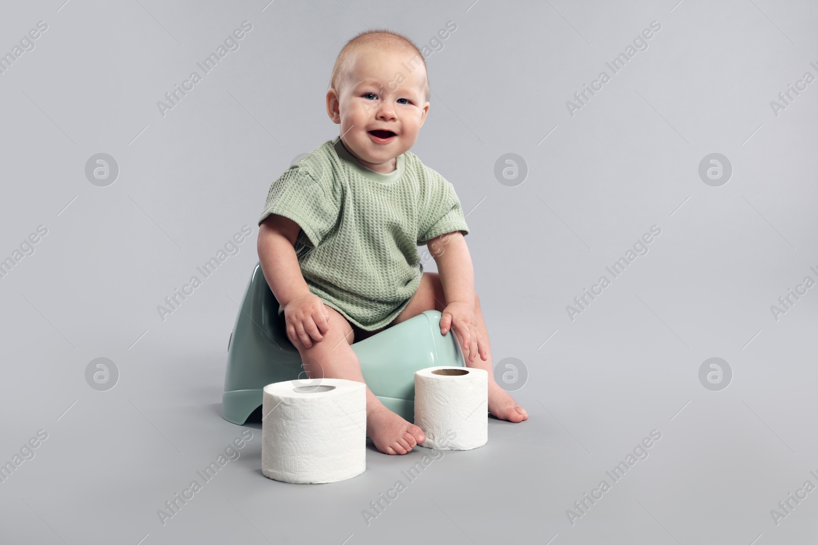 Cute little baby sitting on potty and rolls of toilet paper against light grey background Photo of Cute little baby sitting on potty and rolls of toilet paper against light grey background