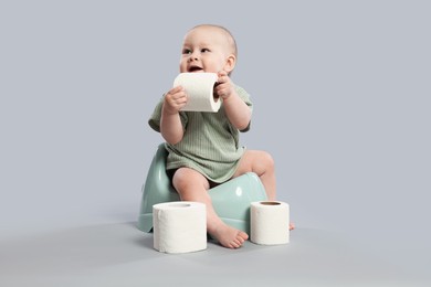 Photo of Cute little baby sitting on potty and rolls of toilet paper against light grey background