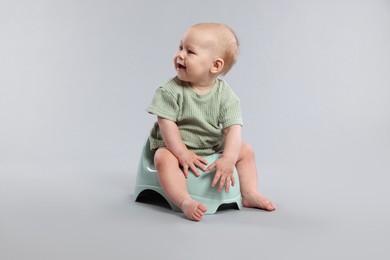 Photo of Cute little baby sitting on potty against light grey background