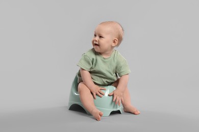 Photo of Cute little baby sitting on potty against light grey background