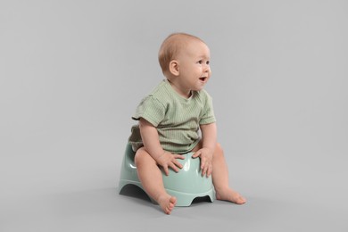 Photo of Cute little baby sitting on potty against light grey background