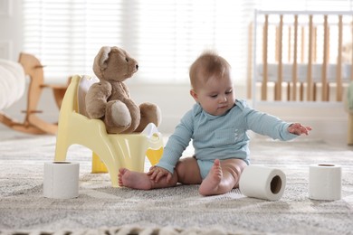Photo of Cute little baby with rolls of toilet paper near potty on floor at home