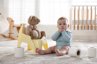 Photo of Cute little baby with rolls of toilet paper near potty on floor at home