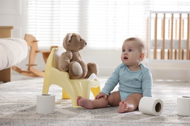Photo of Cute little baby with rolls of toilet paper near potty on floor at home