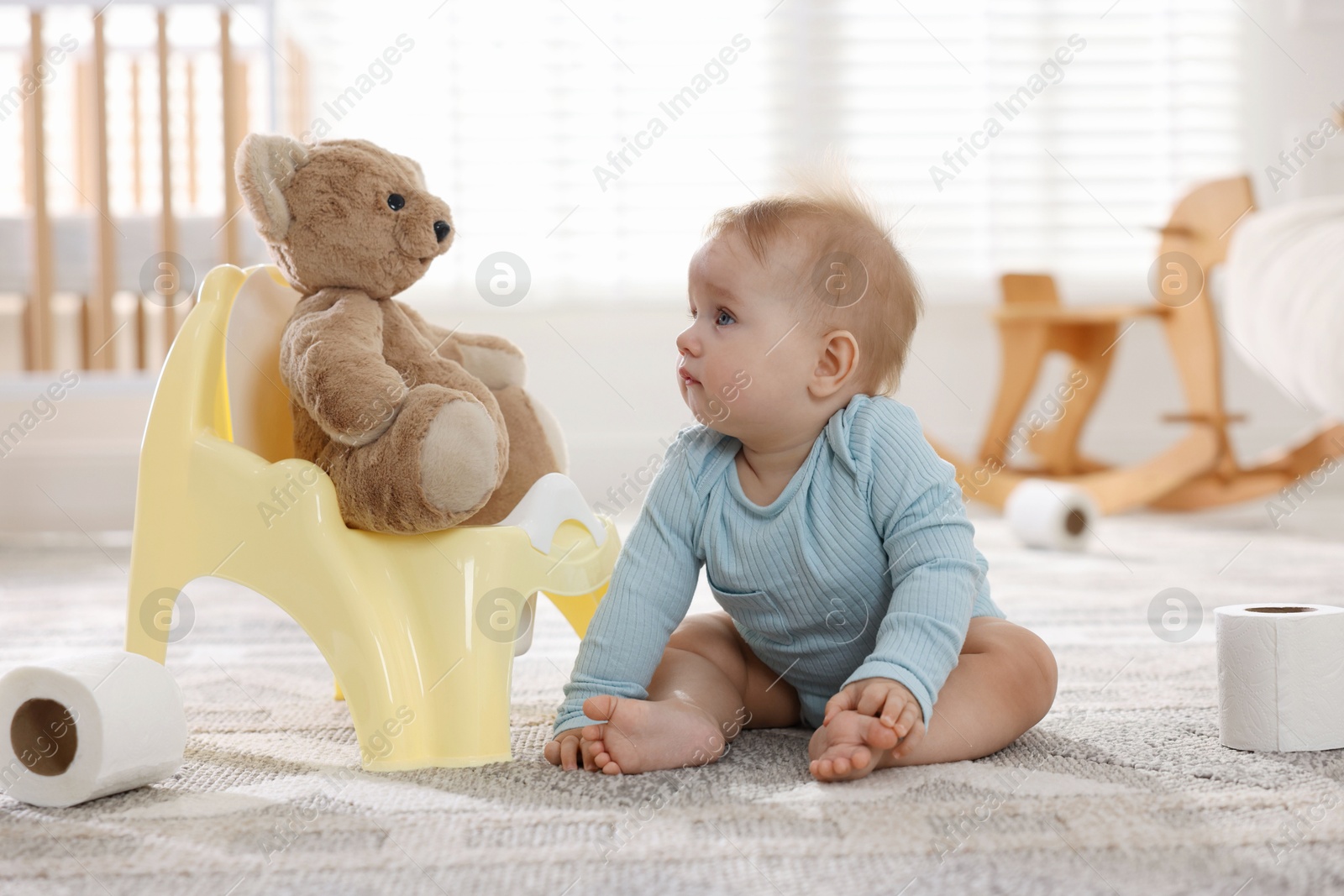 Photo of Cute little baby with rolls of toilet paper near potty on floor at home
