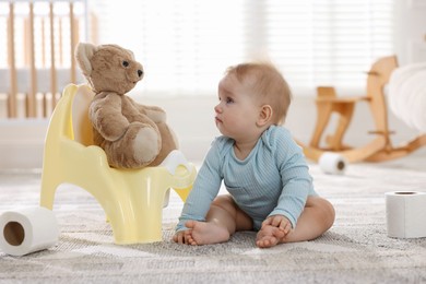 Photo of Cute little baby with rolls of toilet paper near potty on floor at home