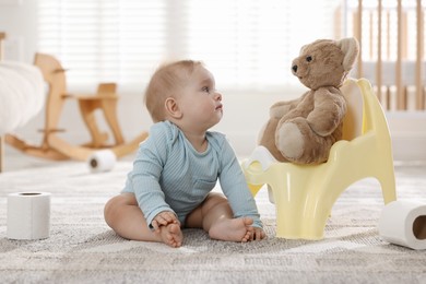 Photo of Cute little baby with rolls of toilet paper near potty on floor at home