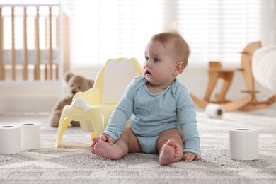Photo of Cute little baby with rolls of toilet paper near potty on floor at home