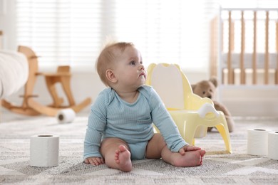 Photo of Cute little baby with rolls of toilet paper near potty on floor at home
