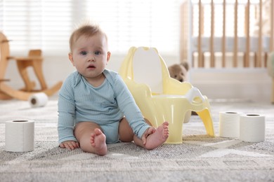 Photo of Cute little baby with rolls of toilet paper near potty on floor at home