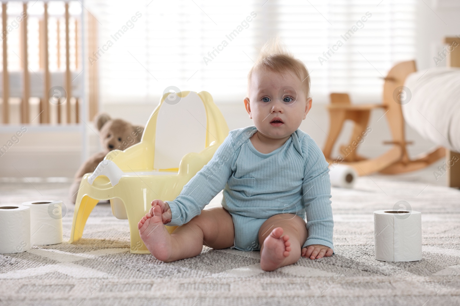 Photo of Cute little baby with rolls of toilet paper near potty on floor at home
