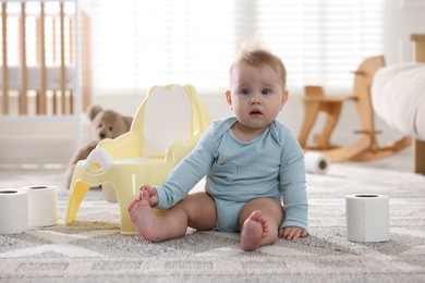 Photo of Cute little baby with rolls of toilet paper near potty on floor at home