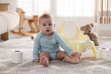 Photo of Cute little baby with rolls of toilet paper near potty on floor at home