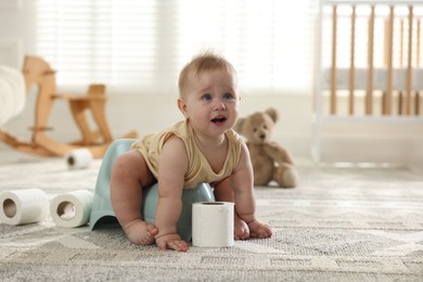 Photo of Cute little baby sitting on potty and toilet paper at home, space for text