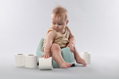 Photo of Cute little baby sitting on potty and rolls of toilet paper against light grey background