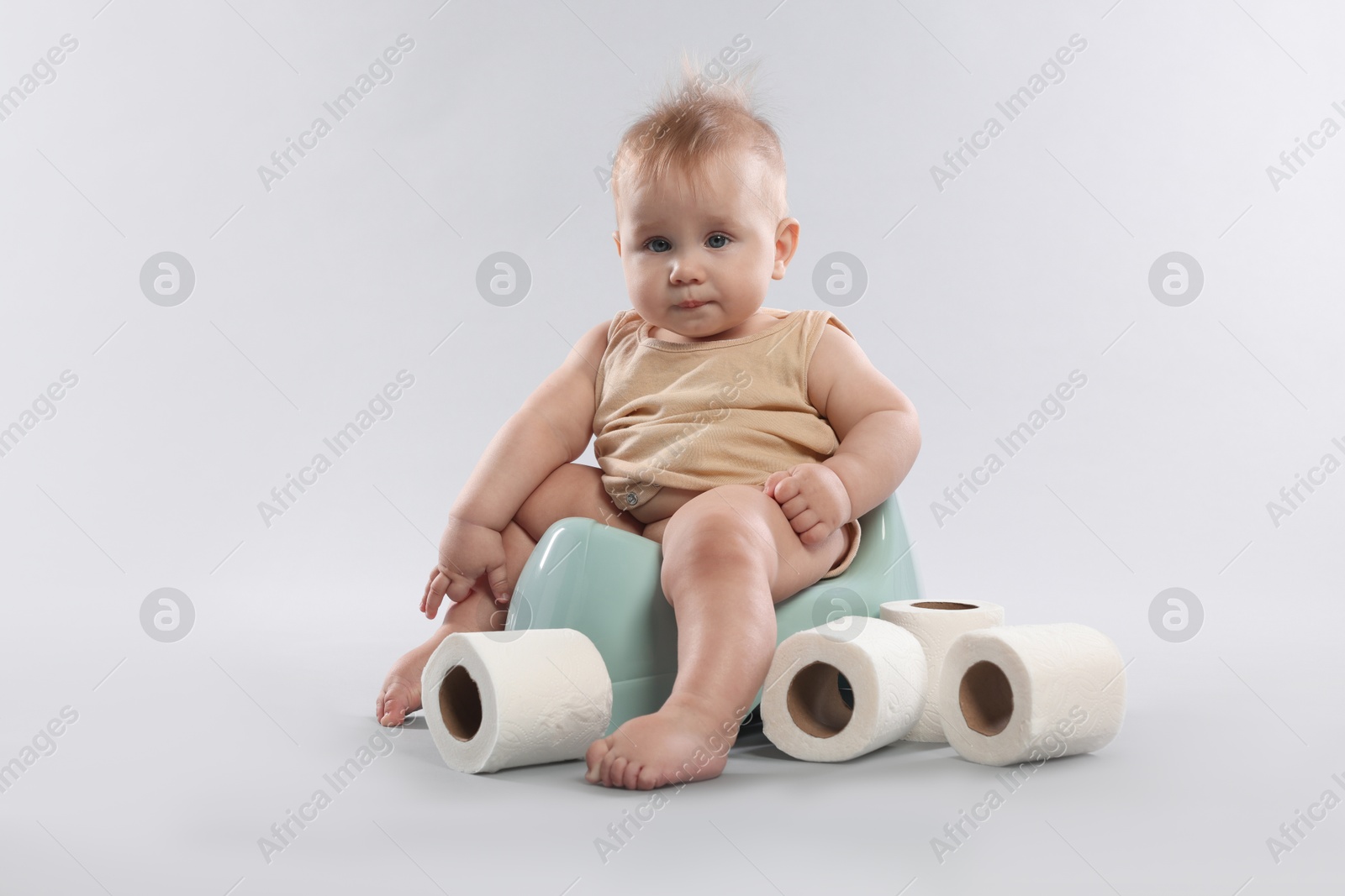 Photo of Cute little baby sitting on potty and rolls of toilet paper against light grey background