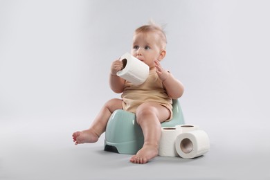 Photo of Cute little baby sitting on potty and rolls of toilet paper against light grey background