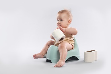 Photo of Cute little baby sitting on potty and rolls of toilet paper against light grey background