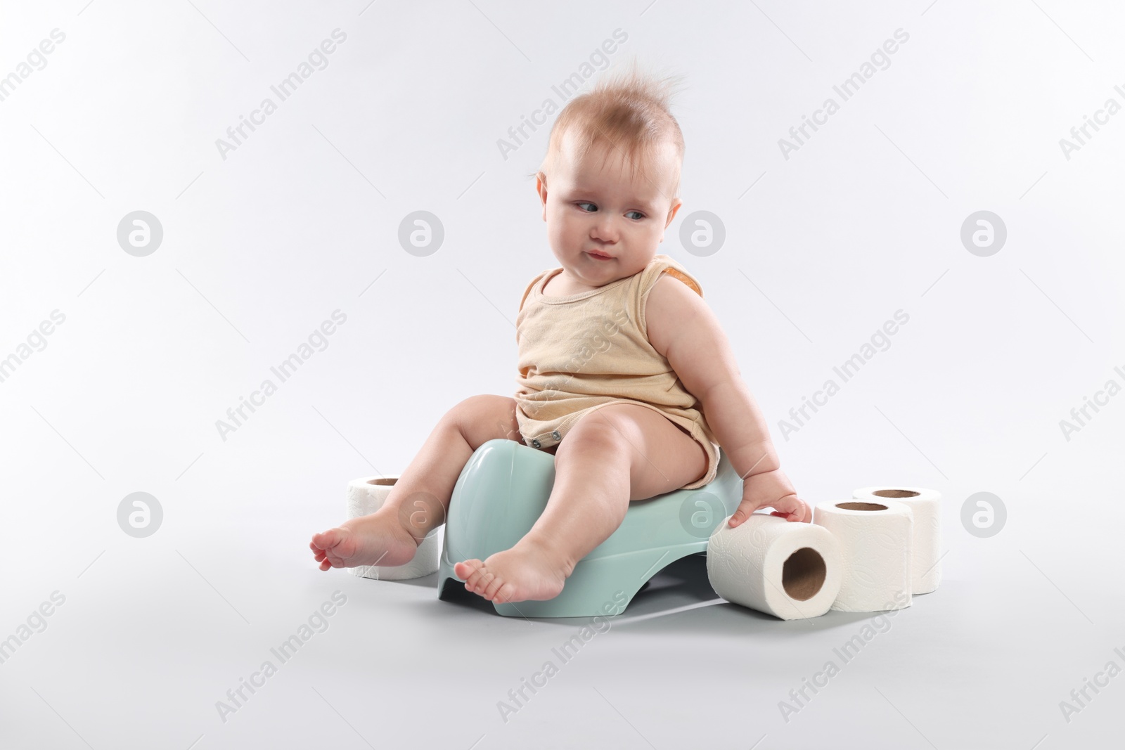 Photo of Cute little baby sitting on potty and rolls of toilet paper against light grey background