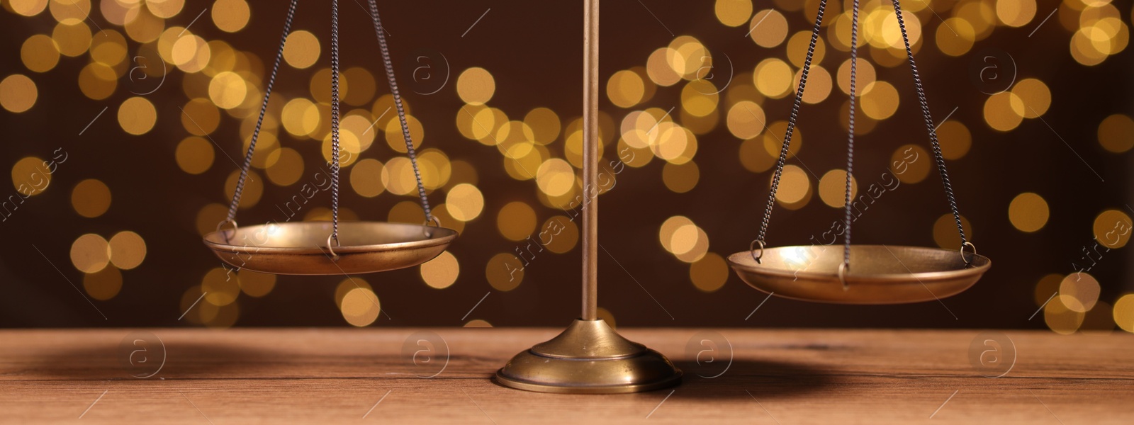 Photo of Golden scales of justice on wooden table against blurred lights, closeup
