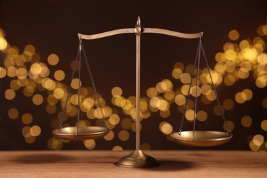 Photo of Golden scales of justice on wooden table against blurred lights