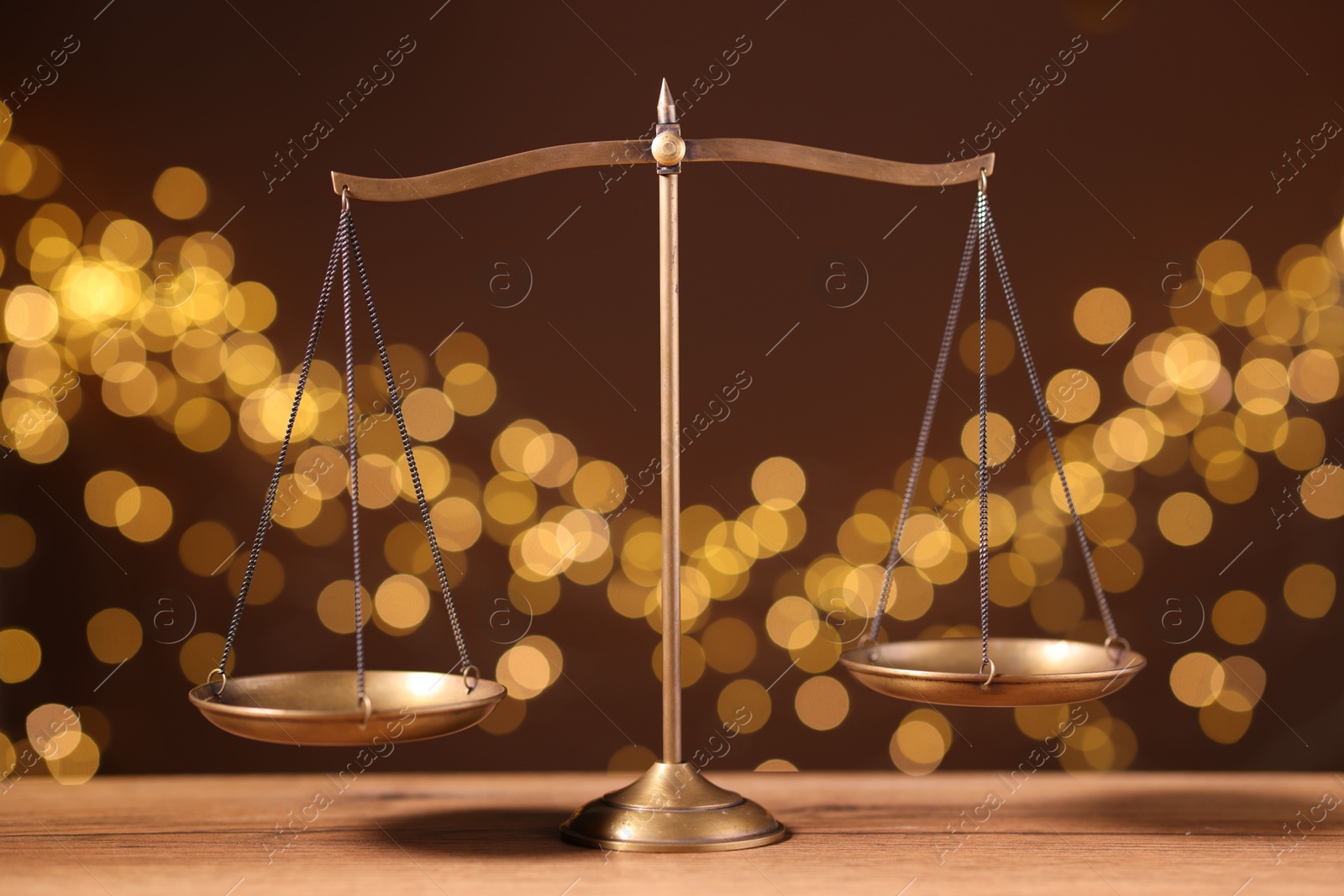 Golden scales of justice on wooden table against blurred lights Photo of Golden scales of justice on wooden table against blurred lights