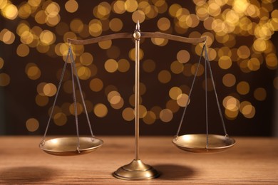 Photo of Golden scales of justice on wooden table against blurred lights