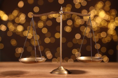 Photo of Golden scales of justice on wooden table against blurred lights