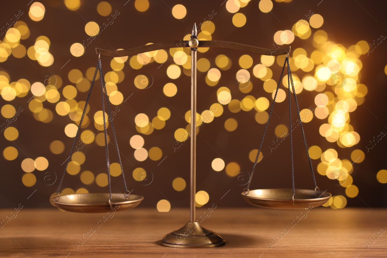 Golden scales of justice on wooden table against blurred lights Photo of Golden scales of justice on wooden table against blurred lights