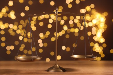 Photo of Golden scales of justice on wooden table against blurred lights
