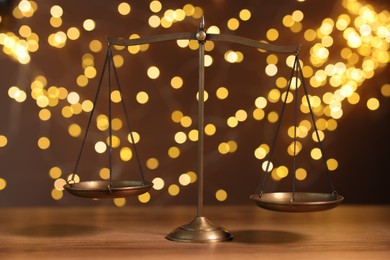 Photo of Golden scales of justice on wooden table against blurred lights