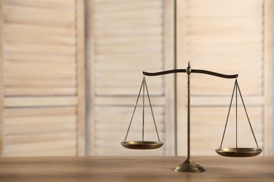 Photo of Golden scales of justice on wooden table, space for text